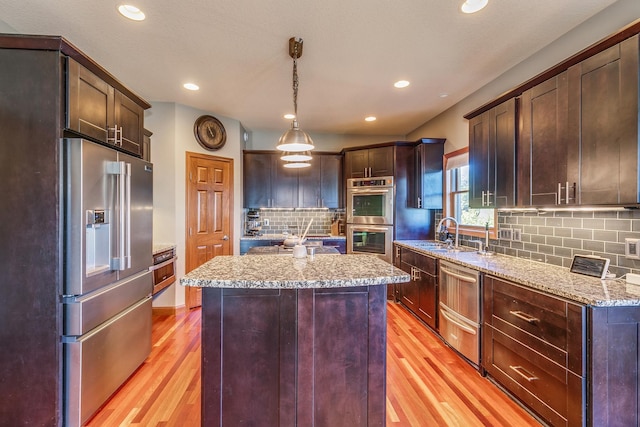 kitchen featuring light stone counters, a sink, a kitchen island, appliances with stainless steel finishes, and decorative light fixtures