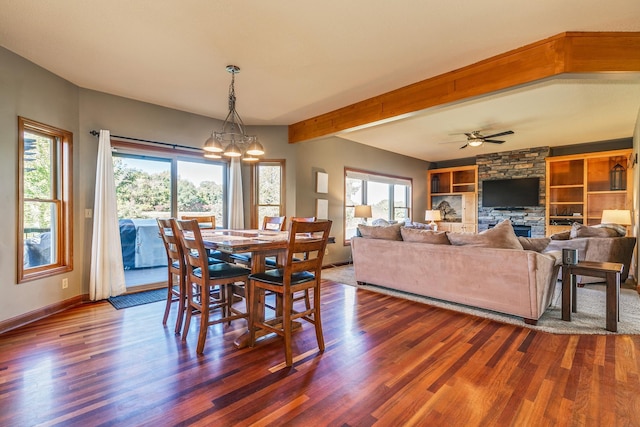 dining space featuring a fireplace, dark wood finished floors, beamed ceiling, baseboards, and ceiling fan with notable chandelier