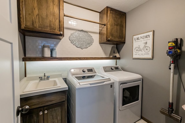 washroom with cabinet space, a textured ceiling, separate washer and dryer, and a sink