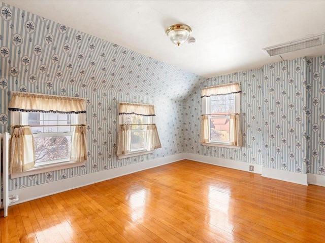 empty room with lofted ceiling, baseboards, hardwood / wood-style floors, and wallpapered walls