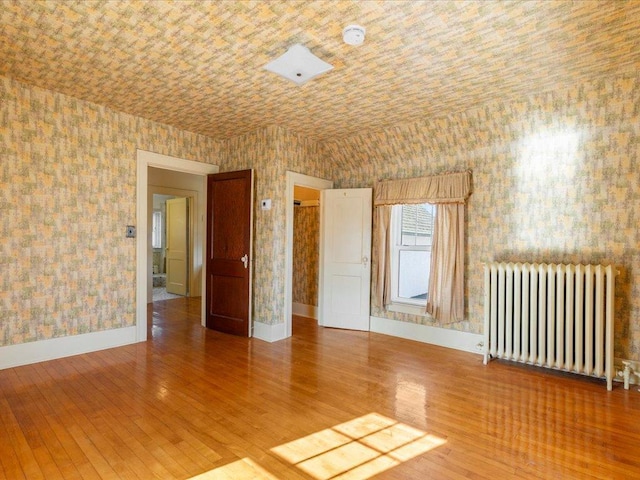 empty room with radiator, hardwood / wood-style flooring, baseboards, and wallpapered walls