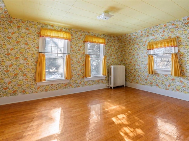 unfurnished room with baseboards, radiator heating unit, hardwood / wood-style flooring, and wallpapered walls