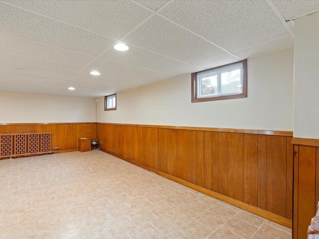 below grade area with a wainscoted wall, wooden walls, a drop ceiling, and a wealth of natural light