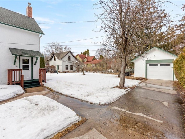 yard covered in snow with driveway, a detached garage, and an outbuilding