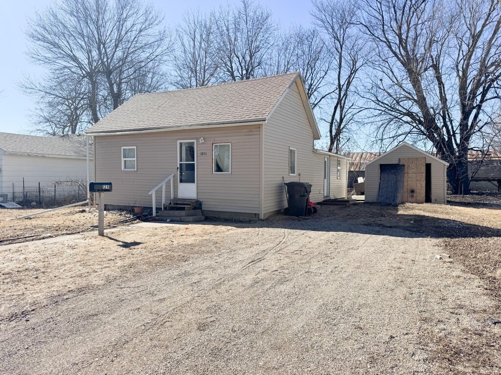 1211 Virginia Ave, Worthington, MN 56187 - view of front of house with a shingled roof, entry steps, driveway, and an outbuilding