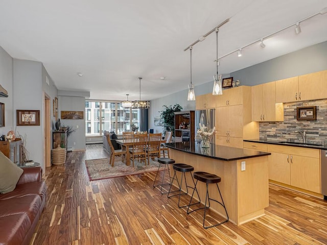 kitchen with dark countertops, open floor plan, a center island, light brown cabinetry, and a sink