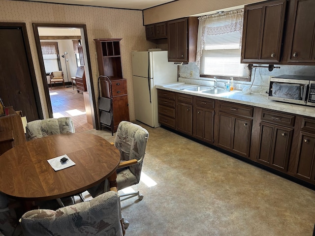 kitchen with stainless steel microwave, freestanding refrigerator, a sink, dark brown cabinets, and wallpapered walls