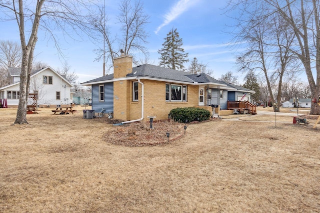 back of house with a deck, roof with shingles, brick siding, central AC unit, and a chimney