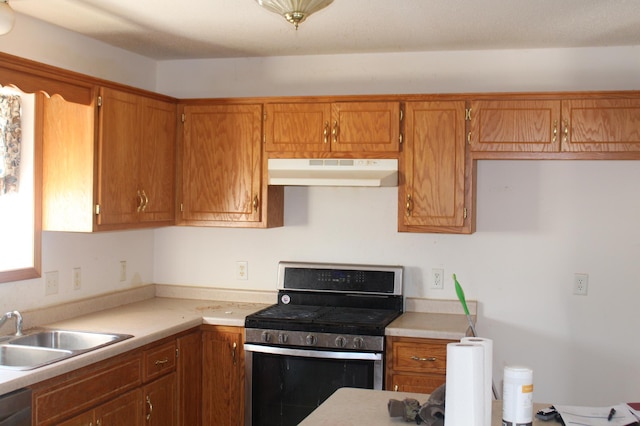 kitchen with light countertops, stainless steel gas range oven, brown cabinets, and under cabinet range hood