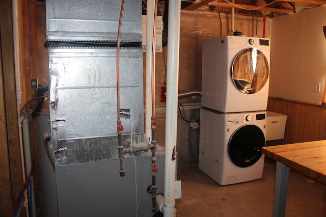 washroom with laundry area, wainscoting, stacked washer / drying machine, heating unit, and wood walls