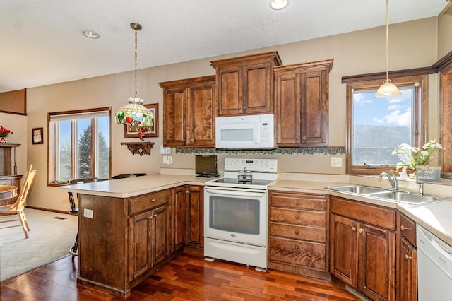 kitchen with a peninsula, white appliances, a sink, light countertops, and decorative light fixtures