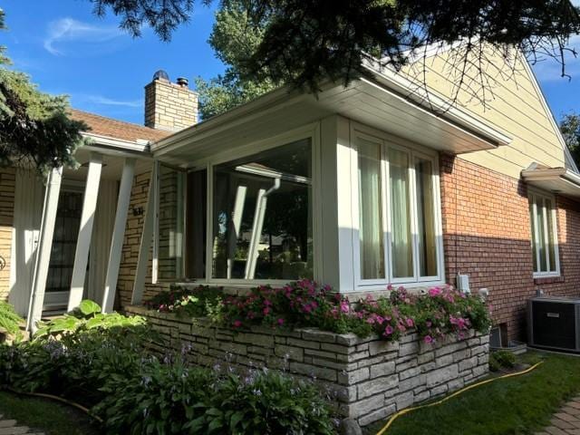 view of side of home with a sunroom, a chimney, cooling unit, and brick siding