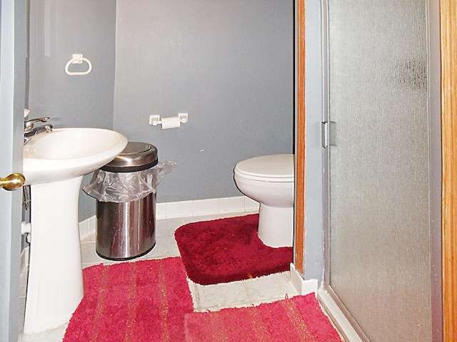 bathroom featuring tile patterned flooring, toilet, a shower stall, and baseboards