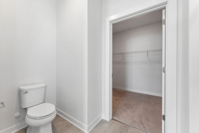 bathroom with a walk in closet, toilet, and baseboards