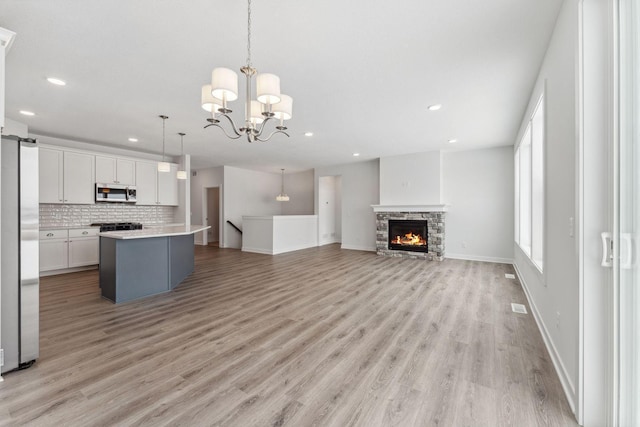 kitchen with open floor plan, stainless steel appliances, light countertops, white cabinetry, and pendant lighting