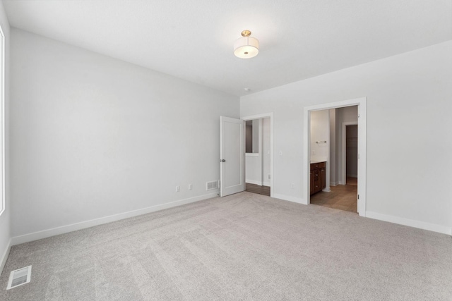 unfurnished bedroom featuring light colored carpet, connected bathroom, visible vents, and baseboards