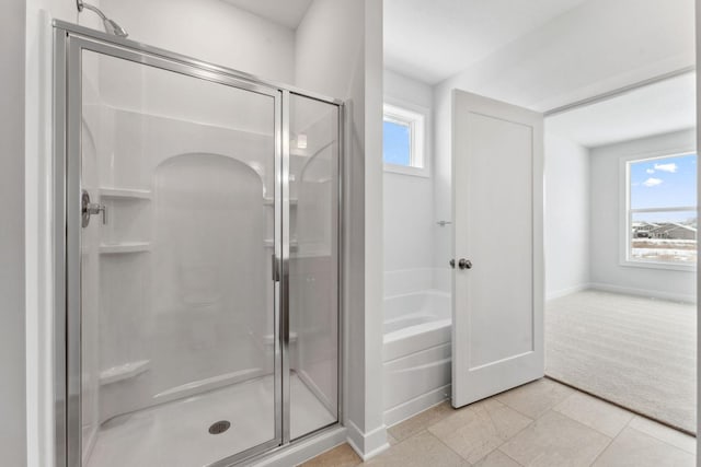 bathroom featuring a stall shower, a bath, and baseboards