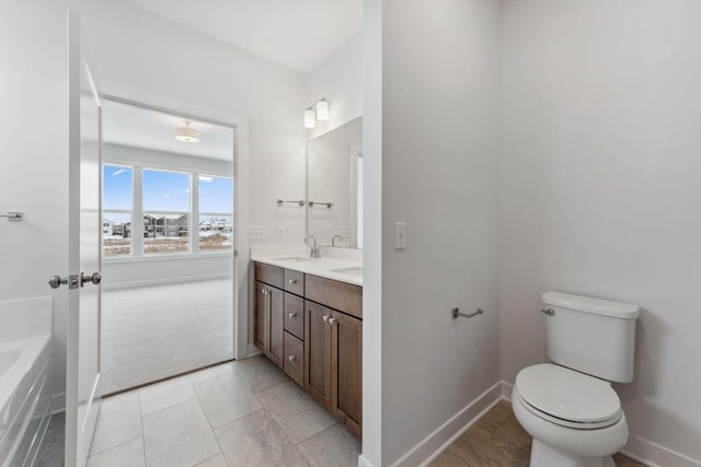 bathroom featuring toilet, a sink, baseboards, double vanity, and a bathtub