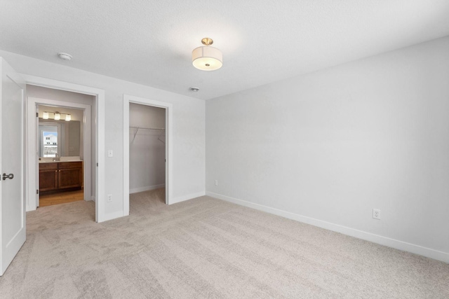 unfurnished bedroom featuring a walk in closet, a closet, light carpet, a textured ceiling, and baseboards