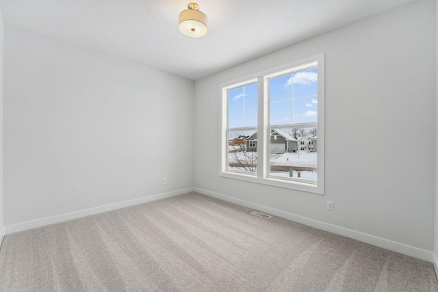 spare room with carpet floors, visible vents, and baseboards