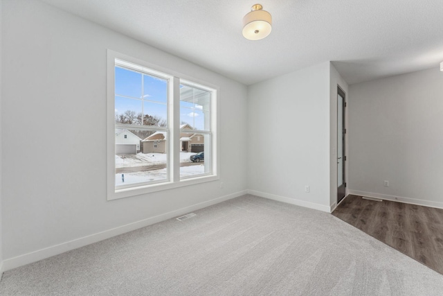 unfurnished room with carpet floors, visible vents, a textured ceiling, and baseboards