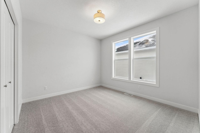 unfurnished room with light carpet, a textured ceiling, visible vents, and baseboards