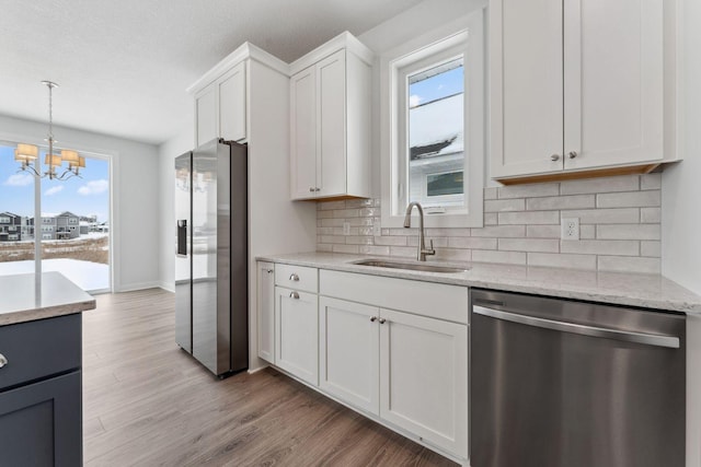 kitchen featuring stainless steel appliances, a sink, white cabinetry, hanging light fixtures, and light wood-type flooring