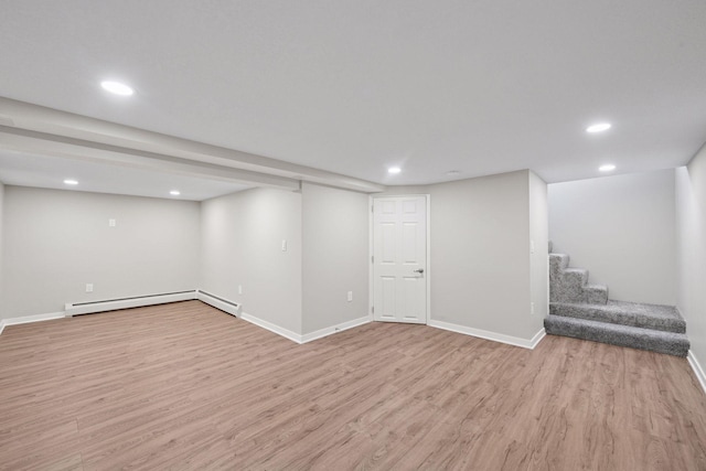 finished below grade area featuring stairs, baseboard heating, recessed lighting, and light wood-style floors