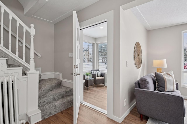 foyer featuring baseboards, stairway, radiator heating unit, and wood finished floors