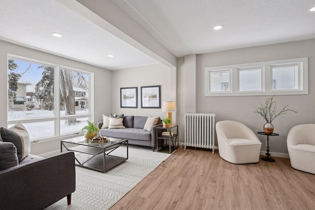 living room featuring baseboards, radiator, a textured ceiling, light wood-style floors, and recessed lighting