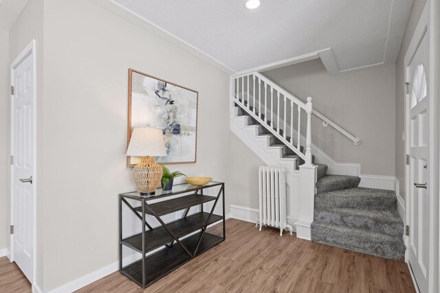 entryway with radiator, stairs, baseboards, and wood finished floors