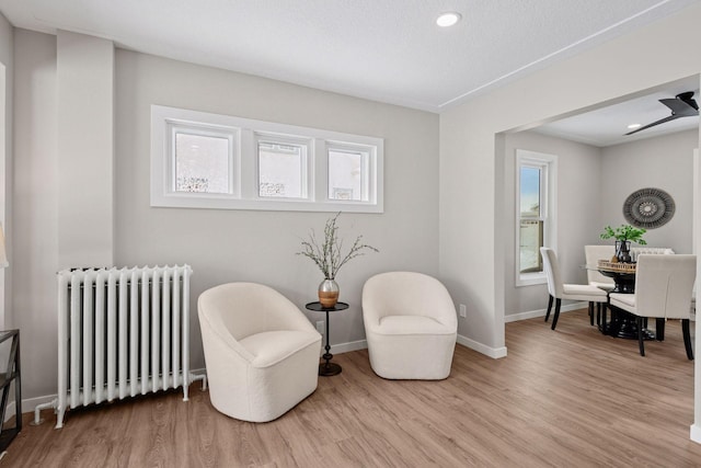 sitting room featuring baseboards, radiator heating unit, a wealth of natural light, and light wood-style floors