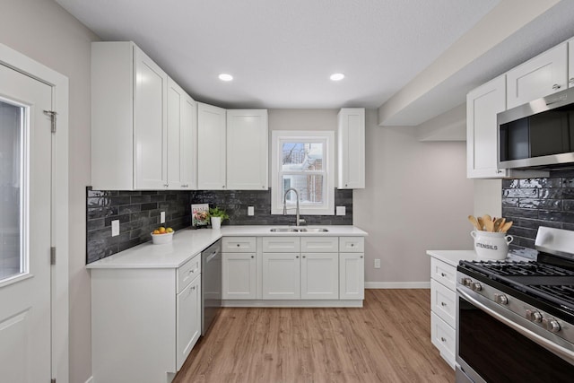 kitchen featuring light countertops, appliances with stainless steel finishes, white cabinets, a sink, and light wood-type flooring