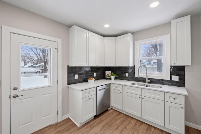 kitchen with light wood finished floors, stainless steel dishwasher, a sink, and white cabinetry