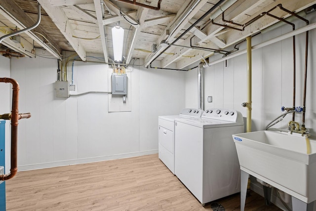 laundry area with laundry area, light wood finished floors, electric panel, washer and dryer, and a sink