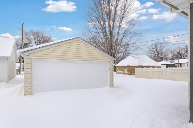 snow covered garage with a garage and fence