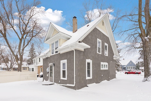 view of snow covered exterior featuring a chimney, fence, and stucco siding