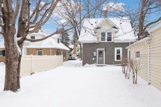 snow covered house featuring fence and stucco siding