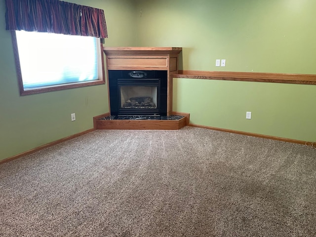 unfurnished living room with carpet floors, baseboards, and a fireplace with raised hearth