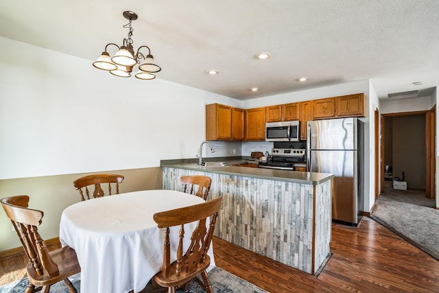 kitchen with decorative light fixtures, dark countertops, appliances with stainless steel finishes, brown cabinetry, and a peninsula