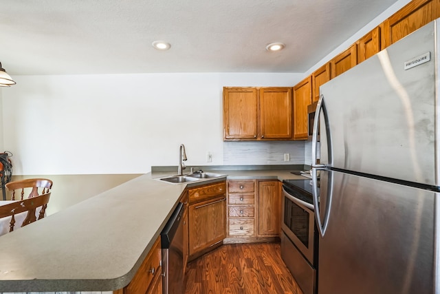 kitchen featuring brown cabinets, dark wood finished floors, appliances with stainless steel finishes, a sink, and a peninsula