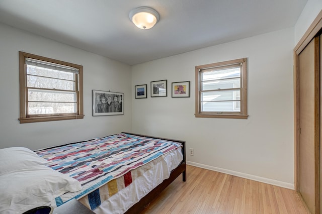 bedroom with multiple windows, a closet, light wood-style flooring, and baseboards