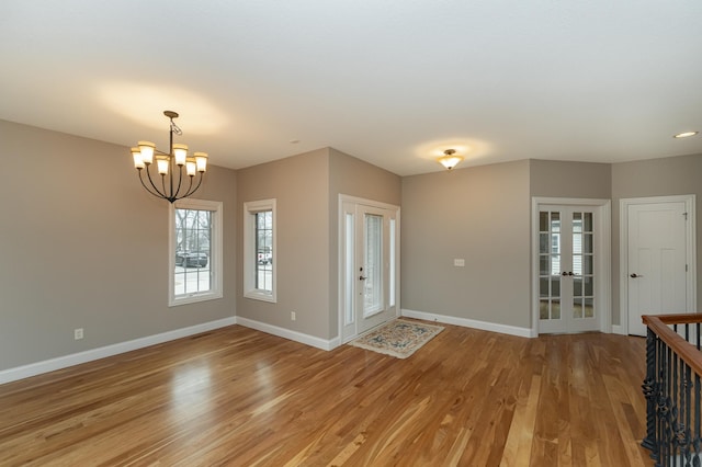 interior space featuring light wood finished floors, baseboards, a notable chandelier, and french doors