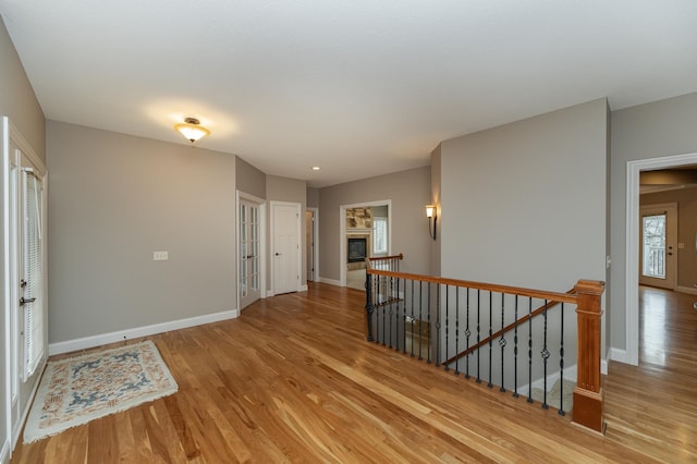 hall featuring an upstairs landing, light wood-type flooring, and baseboards