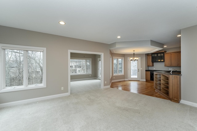 unfurnished living room with baseboards, light colored carpet, a notable chandelier, a sink, and recessed lighting