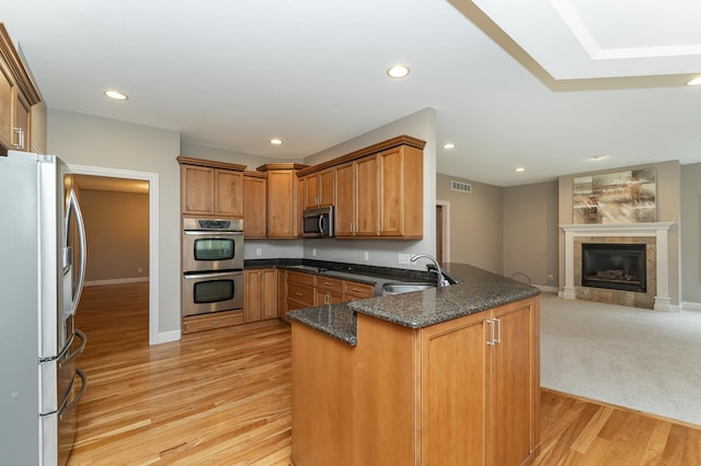 kitchen with a tile fireplace, stainless steel appliances, a peninsula, a sink, and open floor plan