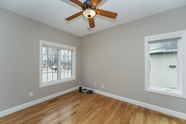 spare room with light wood finished floors, baseboards, visible vents, and a ceiling fan