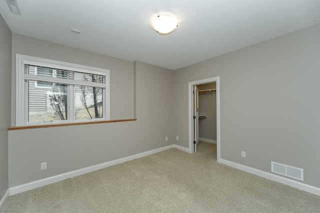 unfurnished bedroom featuring a walk in closet, visible vents, light carpet, and baseboards