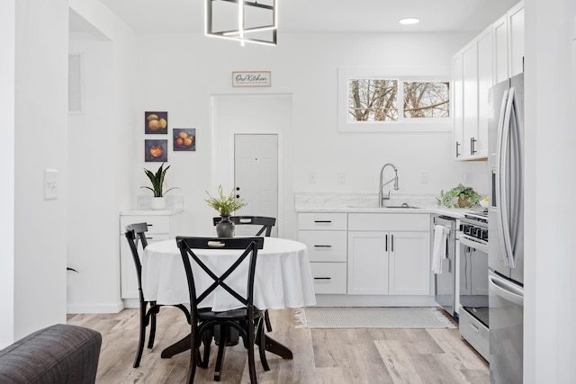 kitchen with stainless steel appliances, light wood-type flooring, a sink, and white cabinets