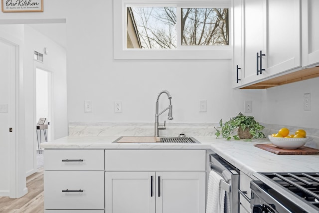 kitchen with light stone countertops, white cabinetry, range, and a sink